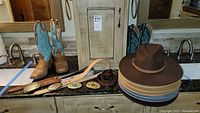 Two pairs of boots, hats, belts and buckles arranged on countertop