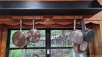 Pan set hanging on rack including stainless steel Wolfgang Puck pans and darker Calphalon pan.