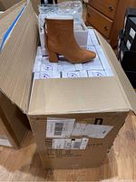 Cards showing a tan faux suede boot displayed on a cardboard box with multiple shoe boxes underneath.