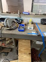 Photo of workbench showing circular saw, plastic bin with nuts and bolts, sanding belts, and wood pieces underneath the bench.
