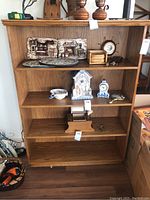 Front view of wood veneer bookcase displaying various decorative items on three of its four shelves.