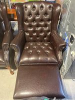 Overall front view of brown pleather wingback chair with matching ottoman in front.