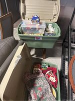 Wide shot of the open green and beige storage bins containing Christmas decor including ornaments, small boxes, and a Christmas-themed figurine.