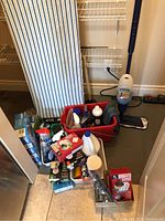 Wide photo of cleaning lot showing ironing board, mop with Bona cleaner, and multiple cleaning bottles in a red tote along with boxed light bulbs on floor.