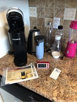 Full lot showing coffee maker, kettle, bottles, blender, and timer on countertop.