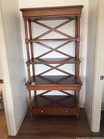 Full front view of tall wooden display shelf with multiple shelves, turned legs, and a bottom dovetailed drawer.