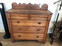 Front view of vintage solid wood dresser showing five drawers with round wooden knobs and scalloped backboard.