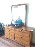 Front view of the wooden dresser with eight drawers and attached large rectangular mirror reflecting light.