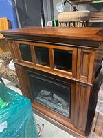 Electric fireplace with wooden mantel showing front view with three glass panels and glass door area with artificial logs inside.