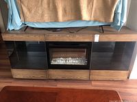 Front view of entire Dimplex electric fireplace cabinet with wood grain finish, glass shelving compartments on each side, and lower drawer.