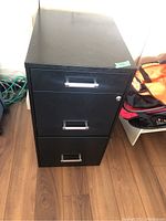 Closed view of the black three-drawer filing cabinet showing metal handles and lock with key