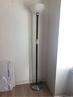 Full view of the floor lamp standing against wall with faux wood flooring.