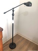 Full view of black vintage style floor lamp standing on wooden floor, showing adjustable arm and round base
