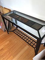 Side angled view of hall table showing black metal frame, glass top and inset slate tiles, floor hardwood visible.