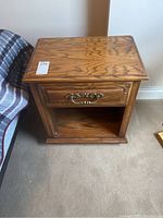 Front view of wooden bedside table showing oak drawer front with brass-style handle and open lower shelf.