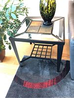 Full view of one end table showing glass and slate tile top, metal frame, and lower grid shelf.