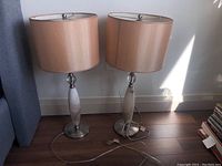 Two matching table lamps with beige fabric shades, oval marble base and brushed metal round base on hardwood floor.