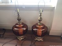 Pair of retro style table lamps with large amber glass bases and ornate metallic feet on wooden floor.