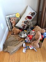 Photo showing various dog-related items including toys, a blanket, a metal dog bowl, a treat dispenser, a pillow with embroidered dogs, and framed dog art.