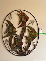 Frontal view of oval steel wall art displaying three angelfish and plant motifs