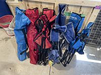 Photo showing six folded camping chairs in various colors and fabric carrying bags, positioned leaning against a wooden pallet wall.