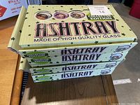 Four stacked unopened boxes of Collector Edition high quality glass ashtrays, green packaging with black stars.