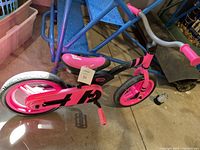 Pink and black Little Tikes balance bike viewed from the side, showing the white tires, pink pedals, pink seat, and black frame with pink accents.
