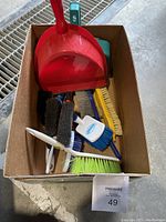 Photo of cardboard box containing assorted brushes, hand brooms, and red plastic dustpan.