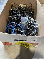Top-down view of a box filled with various cables including power cords, ethernet cables, and HDMI cables.