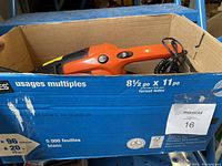 Box containing an orange and black car vacuum plugged in with a coiled power cord