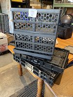 Stack of six black collapsible plastic totes, folded flat, showing circular ventilation holes and overall shape.