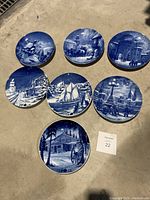 Full set of seven blue and white holiday-themed decorative plates arranged on the ground.