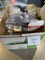 Box with various door handles and hardware including some packaged items and brass finishes