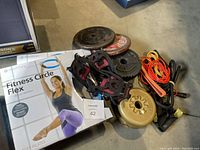Photo shows metal weight plates, boot grips, resistance bands, skipping rope, and boxed Fitness Circle Flex pilates ring