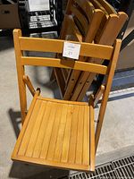 Four wooden folding chairs stacked and folded showing the seat and backrest detail.