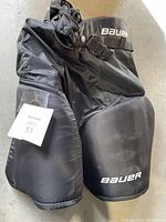 Black Bauer hockey pants folded, showing front with Bauer logo and waist buckle.