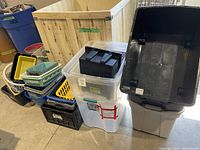Large assortment of plastic bins, totes, and baskets stacked on a floor including clear totes with lids, black crates, and smaller baskets in various colors.