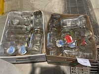 Photo showing two open cardboard boxes filled with clear glass mason jars in various sizes, some with metal lids, some without.