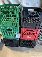 Stack of six plastic milk crates in green, black, and red colors showing front and sides with label tags.