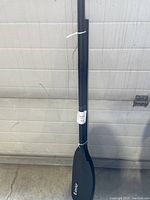 Full length view of the sports paddle leaning against a wall, showing the shaft and blade shape.