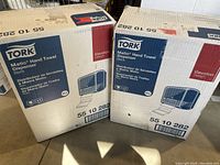 Two stacked boxes showing Tork brand Matic Hand Towel Dispensers in black color, original packaging.