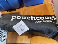 Black carrying bag labeled 'pouchcouch pouchcouch.ca' with a MaxSold tag number 41 on it, lying flat on a wooden floor.