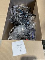 Box of new safety goggles in various styles and frames photographed from above, showing multiple goggles packed loosely.