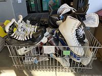 Top view of wire basket filled with multiple pairs of black hockey skates and white figure skates in assorted sizes.