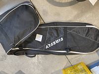 Full view of the black Firefly ski bag laid flat on a floor, displaying its overall shape and size.