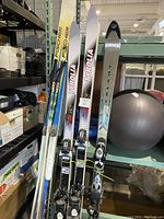 Four pairs of skis standing upright on a shelf next to a black exercise ball.