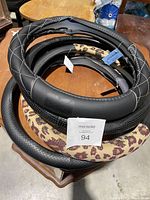 Photo of the 4 steering wheel covers stacked showing different designs including quilted black, leopard print, and black textured covers.