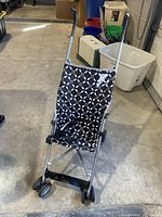 Front view of lightweight umbrella stroller with black and white geometric seat fabric, foldable metal frame, and double wheels.