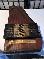 Top-down photo showing entire zither, strings, tuning pegs, and black decorative faceplate measuring about 20 inches by 12 inches.