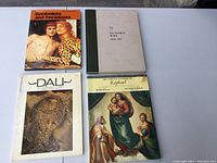 Four art books laid out flat on a concrete surface showing cover titles and art images.